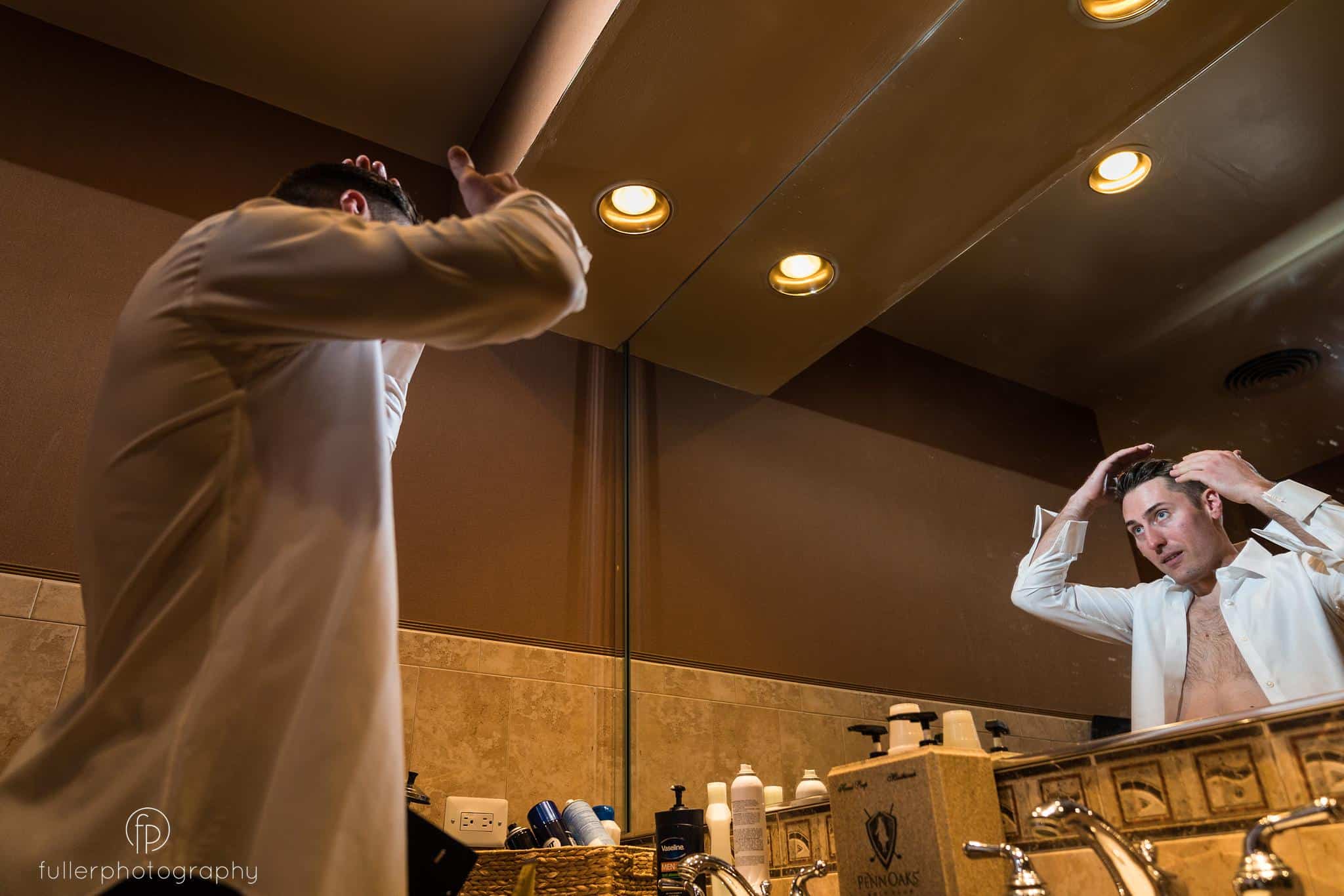 Groom styling his hair in a mirror in the Penn Oaks locker room