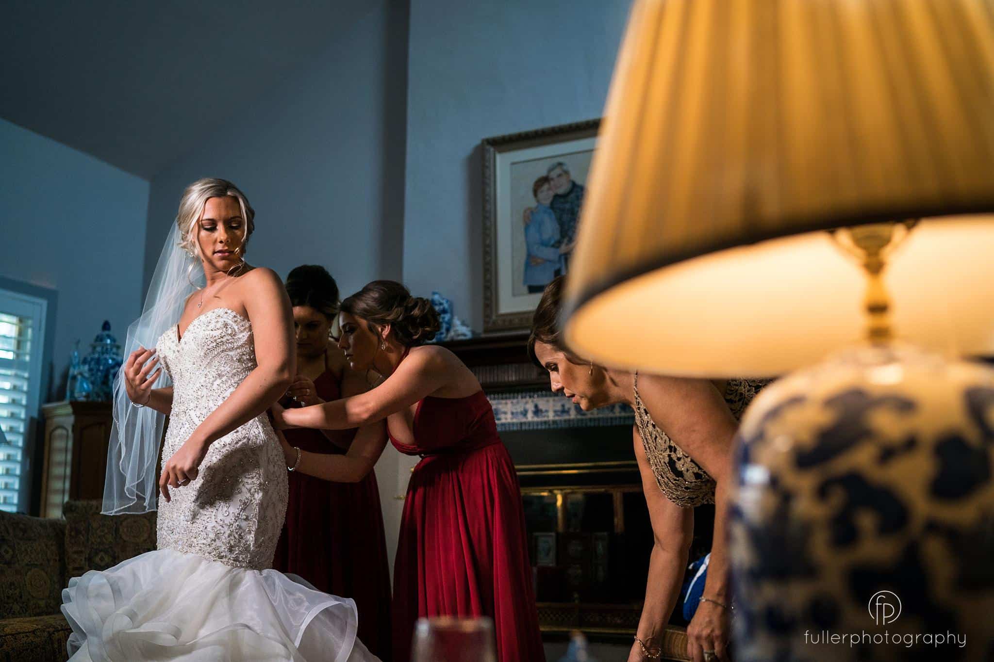 Bridesmaids helping the bride get ready by buttoning up her dress