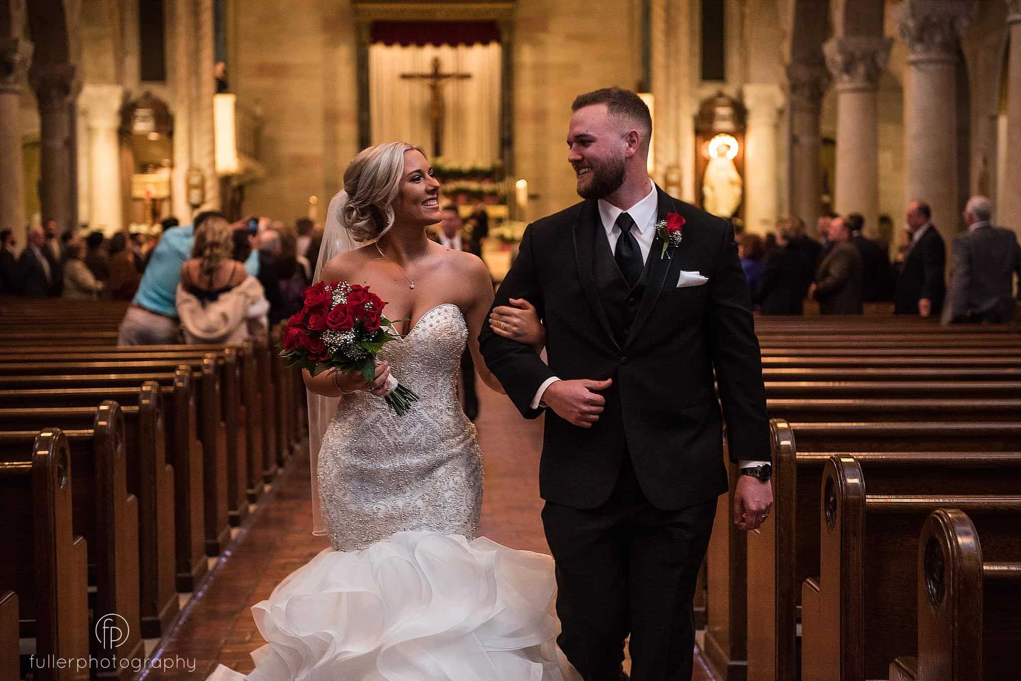 Bride and groom smiling at each other as they walk down the isle after becoming husband and wife