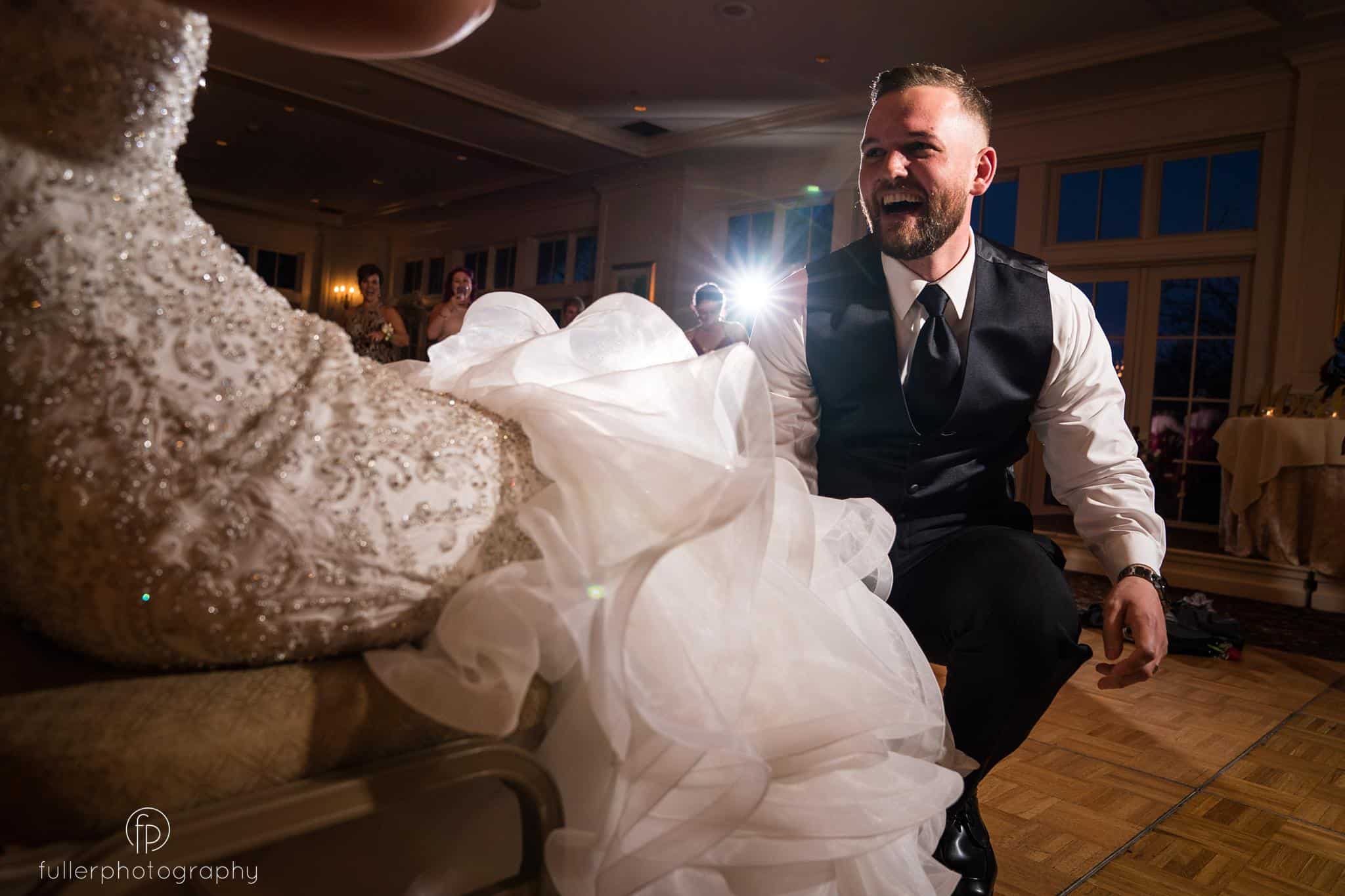 The groom laughing and kneeling as he's about to take off the garter from his wife's leg