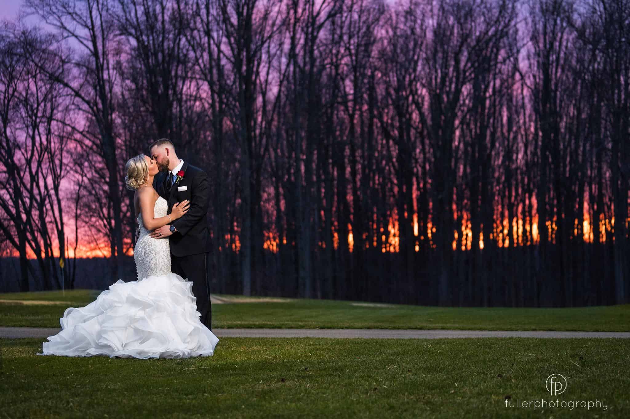 The bride and groom kissing in front of an amazing sunset during their Wedding Reception at Deerfield Golf Club Golf