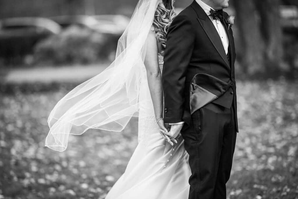 Bride and groom holding hands while the wind takes the veil during their White Manor Country Club Wedding
