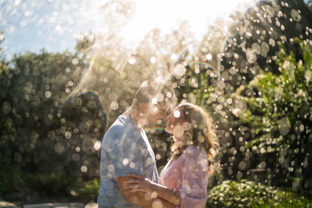 Couple under a sprinkler at Marian Coffin Gardens during their engagement session